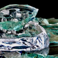 A small bench made of green glass with 4 legs of smokey shattered glass, sits atop a scattering of broken glass rocks